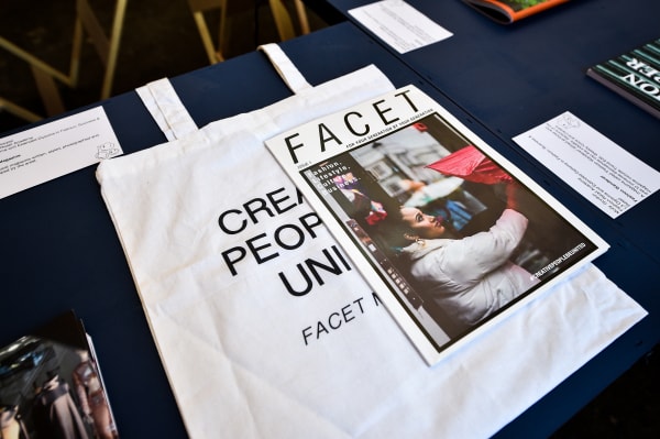 Table with white tote bag with few words on and a magazine called ‘Facet’ 