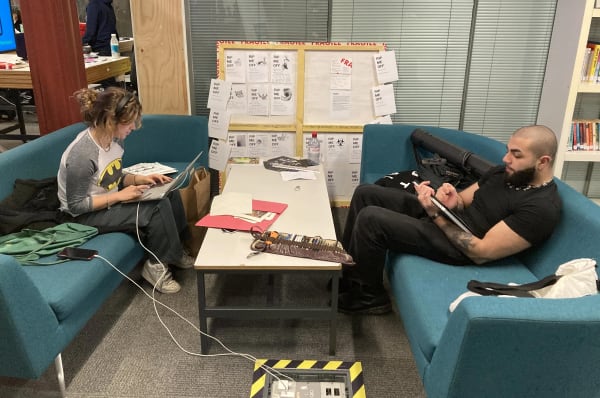 Two people sitting on opposite sofas working on laptops, with a table in the middle.