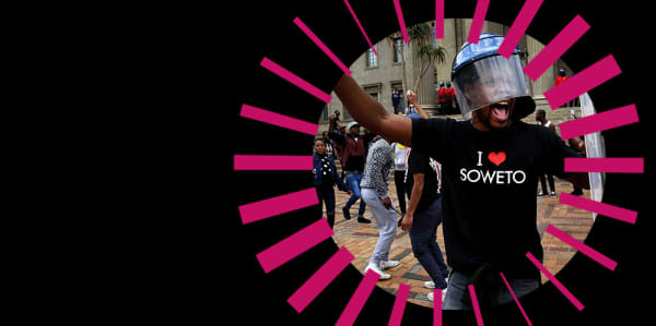 A man, wearing a helmet and a t-shirt reading I love Soweto,shouting inside a pink radial graphic on a black background