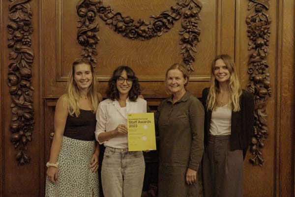4 people stood in front of an ornate wood wall, the people are smiling and the person in the middle is holding a yellow printed certificate with text 'Knowledge Exchange Staff Awards 2023'