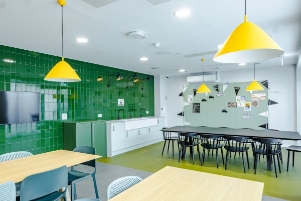 View of a spacious common room with multiple tables and chairs, alongside kitchenette / bar area with sink access.