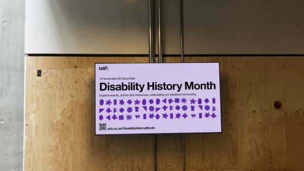 A large, horizontal digital screen displays purple symbols and text. The UAL logo is in the top left, followed by black text that reads 'UAL Disability History Month, 14 November to 20 December. Explore events, stories and resources celebrating our disabled community.' Below the text are dozens of purple cut out shapes forming 3 long lines that stretch across the width of the screen. Underneath the shapes is a QR code and a URL that reads 'arts.ac.uk/DisabilityHistoryMonth.'