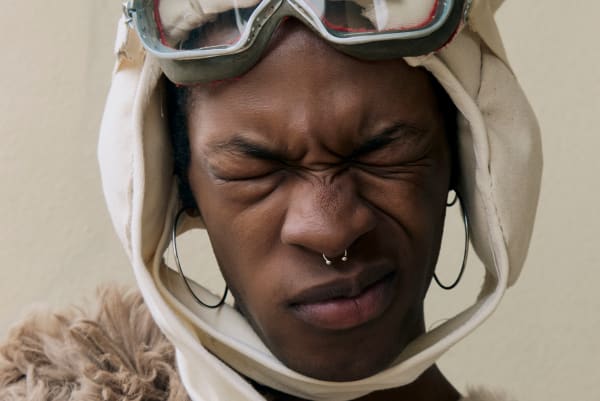 Model wearing goggles and headwear with eyes closed.