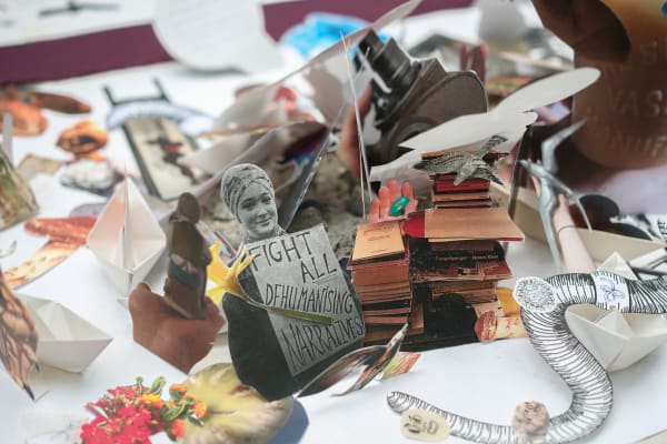 A colourful collage work, at its centre is a black and white portrait of a person holding a sign stating 'Fight all dehumanishing narratives'