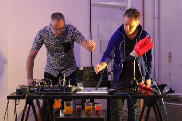 CRiSAP researchers Mark Peter Wright and Angus Carlyle giving a sound performance, using microphones, beakers of liquid, a rubber glove and other objects.