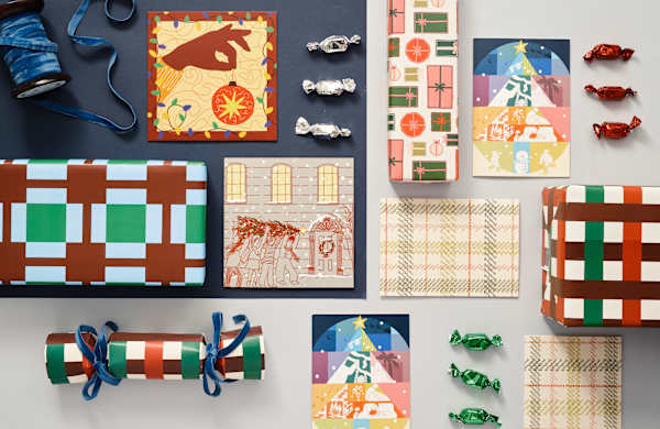 Festive flat lay with patterned holiday cards, wrapped gifts, ribbon, and colorful candies on a neutral background. Vibrant, cheerful tones.
