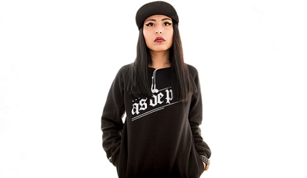model posed in a black logo crew neck top and hat, against a white backdrop. Wired headphones hang out of model's top.