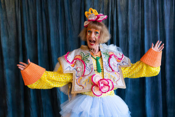 Grayson Perry poses for a picture with his arms raised, wearing his 2022 graduation robe.