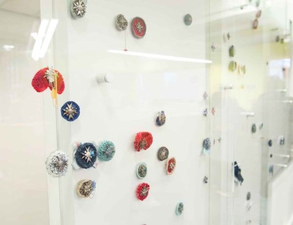 Knitted brooches with metallic details arranged on a glass wall