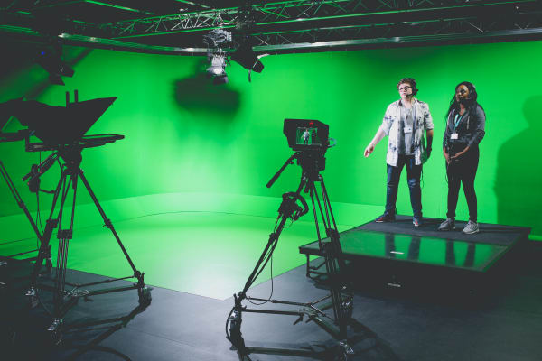 Image of 2 students in a green screen setting, in front of a camera