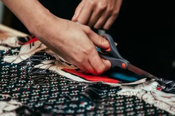 Person cutting colourful fabric with scissors.