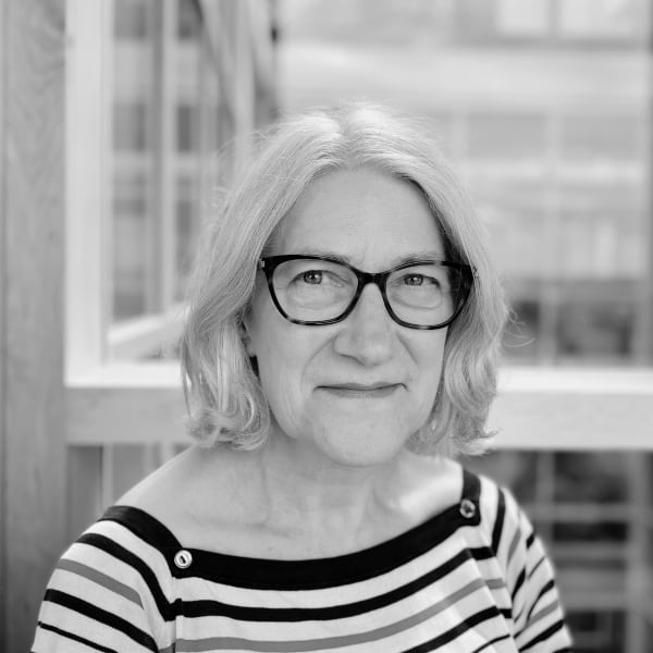Sheila Clark, wearing glasses and smiling at the camera wearing a striped top