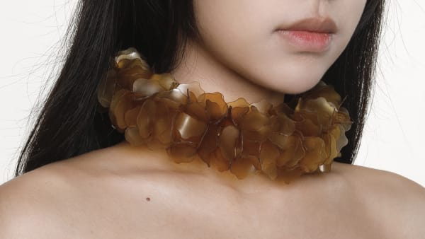 A close-up landscape shot of a coral-coloured necklace made of bio-plastic worn on a body, with shoulders, top of chest, chin and mouth visible.