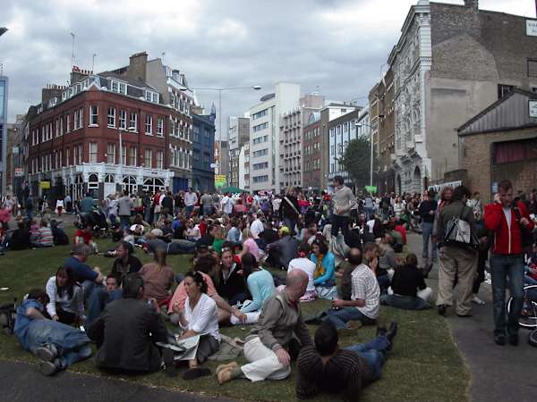 A large group of people sitting and lying down on the grass in a city square