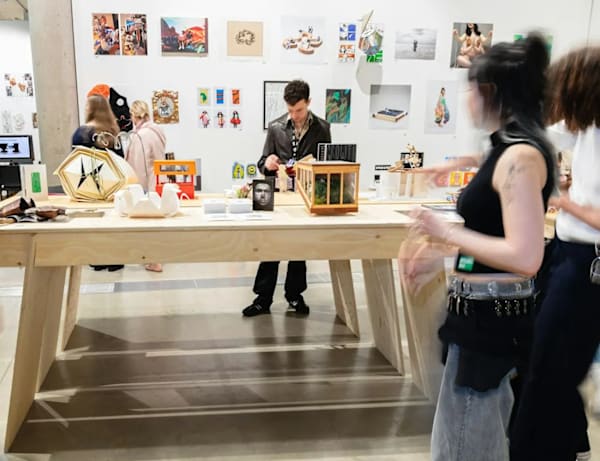 Audience viewing an exhibition, there are a number of people standing around a table looking at 3D objects and models 