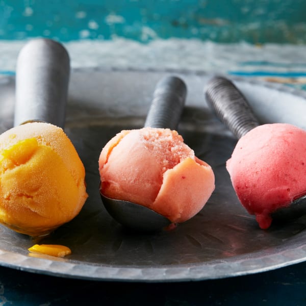 Three ice cream scoops side by side each holding with a different colour sorbet 