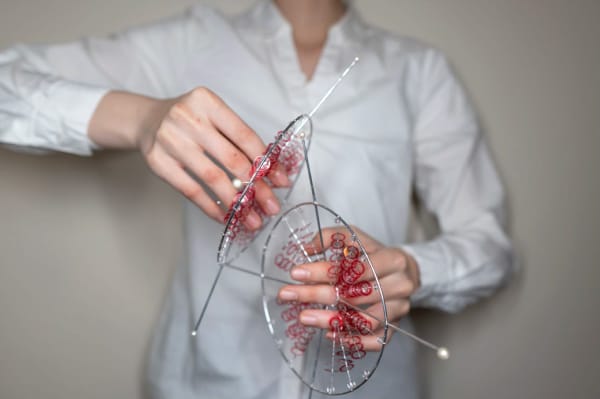 Hands holding perspex and red thread appendages