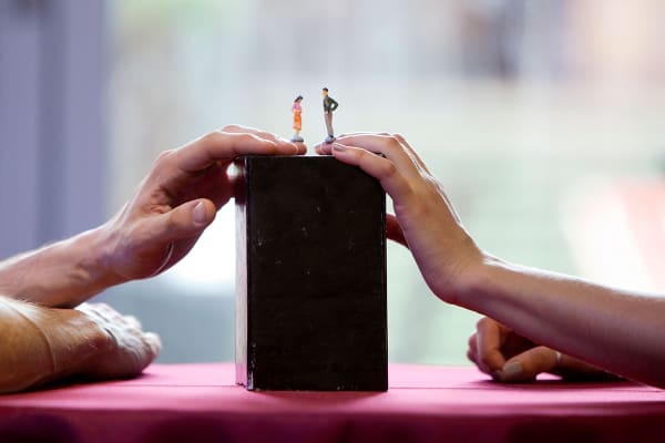 Two hands holding small model people one female and one male on top of a black tall rectangular box as part of a workshop by ZU-UK.