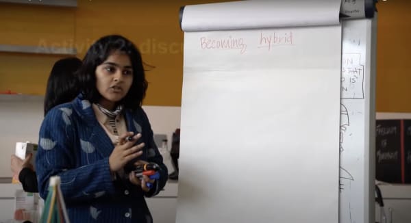 A student presenting next to a flipchart page with handwritten title 'Becoming Hybrid'