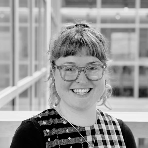 Lucy Graham, wearing clear glasses and a black and white checked dress, smiling at the camera
