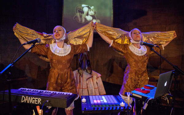 Actors dressed as angels behind keyboards, mixer, microphones and laptop.