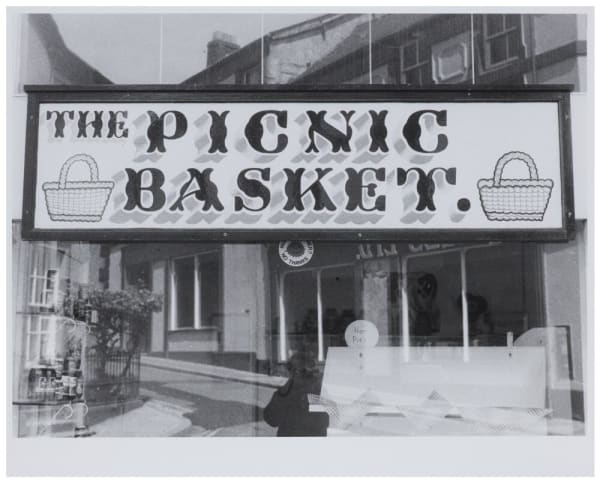 Black and white photograph of a sign in a shop or café window, reading, ‘The Picnic Basket’