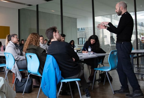 Students sat down listening to a teacher who is standing
