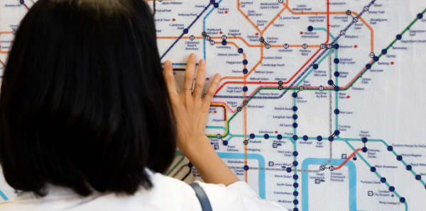 Female student seen from behind with hand reaching up to read braille London Tube map