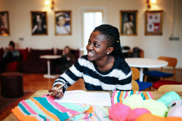 Student at a desk with textiles, smiling.
