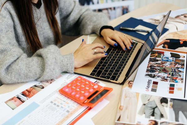 Woman on a laptop with a calculator beside her, MA Fashion: Buying and Merchandising (now PG Cert Fashion: Buying and Merchandising), Zoe Zanon Rives in the studio