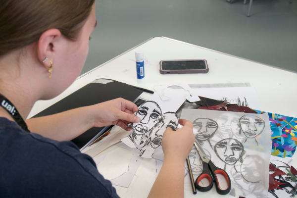 A student holding two cutouts of faces drawn on paper