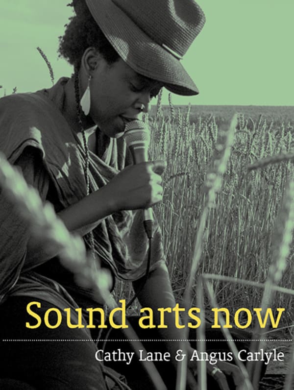 Book cover of Sound Arts Now by Cathy Lane and Angus Carlyle.  The cover features a person sitting in a cornfield speaking into a microphone.