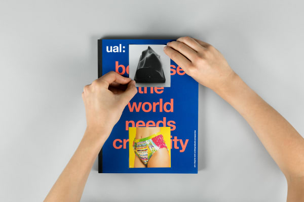 Hands placing a second square sticker over the title of the 2018 undergraduate prospectus, the placement of 2 stickers creates the brandmark on the cover of the prospectus.