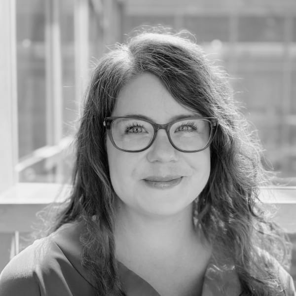 Claire Bunyan, Senior Research Fellow in Cultural Anthropology, is smiling at the camera and wearing a pair of thick framed glasses