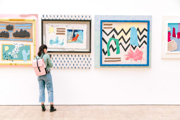 A person looking at two artworks hugn on a white wall