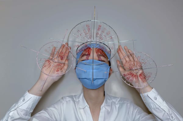 Figure wearing surgical mask and perspex and red thread appendages