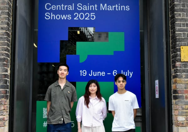three students designers outside the CSM gallery. Two men and one woman. They're standing in front of the CSM gallery window that displays graphic imagery of the CSM shows 2025.