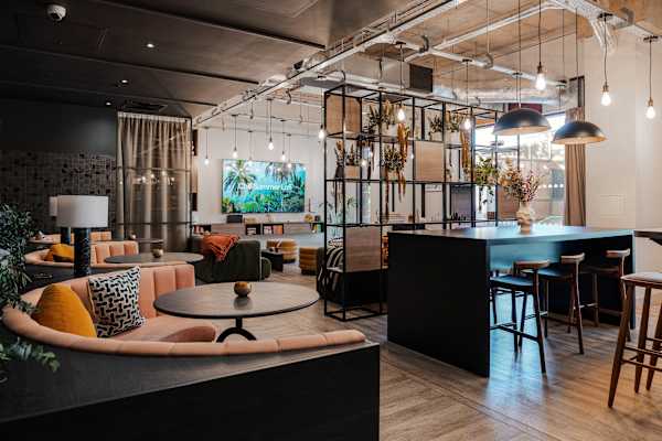 A lounge with curved sofas, small tables and dining area seating. Lots of ceiling lighting and lamps.