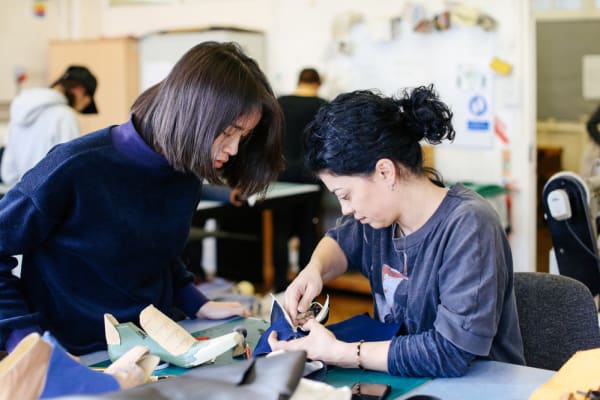 Two female students in a workshop leaning over a piece of work with tools in hand