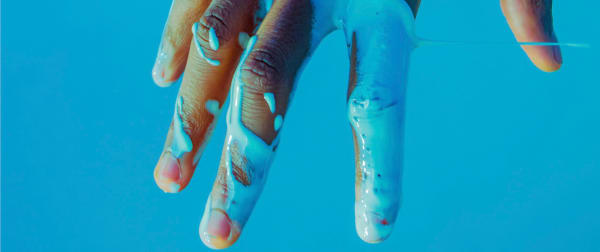 A hand covered in blue paint, against a blue background.