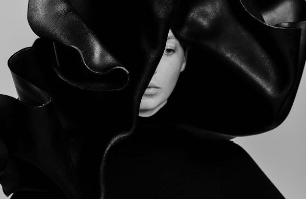 Black and white image. Female model in large, black hat covering half of her face.