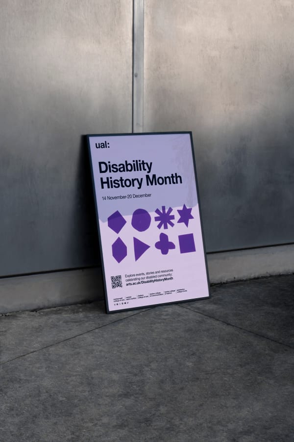 A frame displaying an A2 poster leans against a metal-clad wall. The poster features a diverse arrangement of purple shapes and reads 'UAL Disability History Month, 14 November to 20 December, Explore events, stories and resources celebrating our disabled community: arts.ac.uk/DisabilityHistoryMonth.' alongside a QR code. There is a list of UAL colleges and social media icons running along the bottom of the poster.