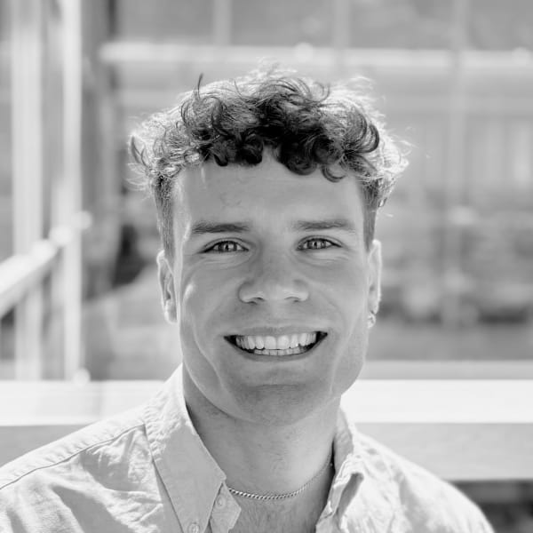 Freddie O'Reilly, Senior R&D Fellow in XR Textiles and Dress, wearing a white shirt, and smiling at the camera, in a black and white photo with a plain white background