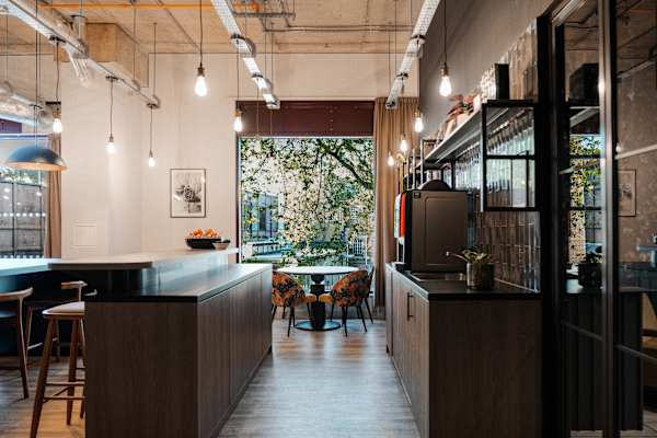 Dining and kitchen area with black cupboards and shelving. Dining table near the window and a breakfast bar with high seats. Sink and coffee area. 