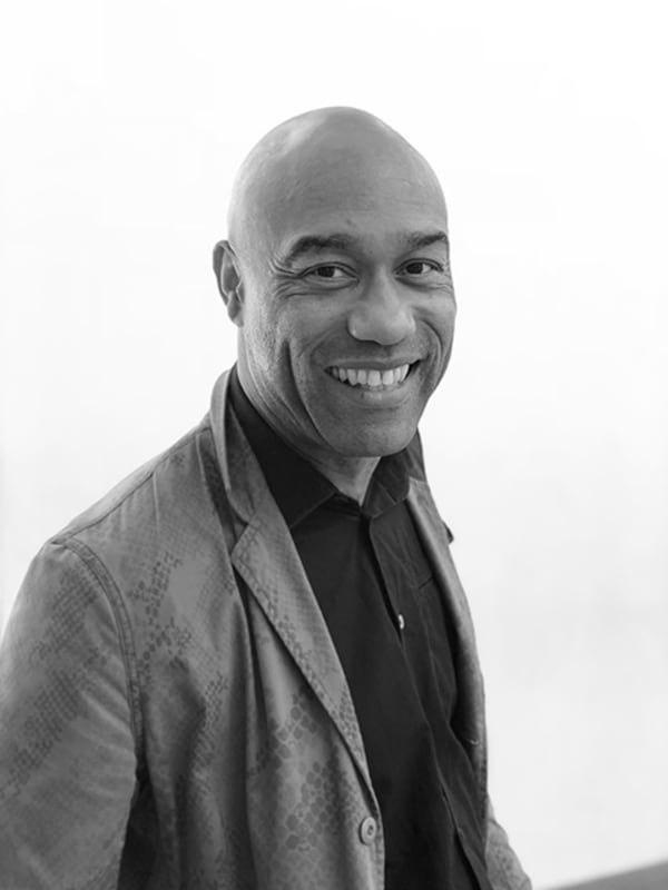 Black and white portrait of Dr Gus Casely-Hayford smiling at the camera from a side angle
