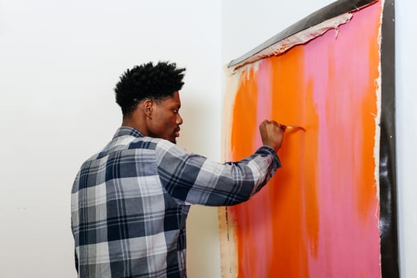 A student painting a canvas with bright pink and orange hues.