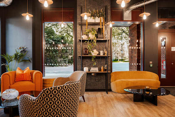 Reception area with lots of lighting, sofa seating and a low table. Shelving unit on the wall in between two large windows.