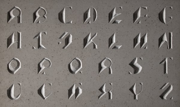 A slab of wood hand engraved with a custom typeface inspired by historical tombstone lettering.