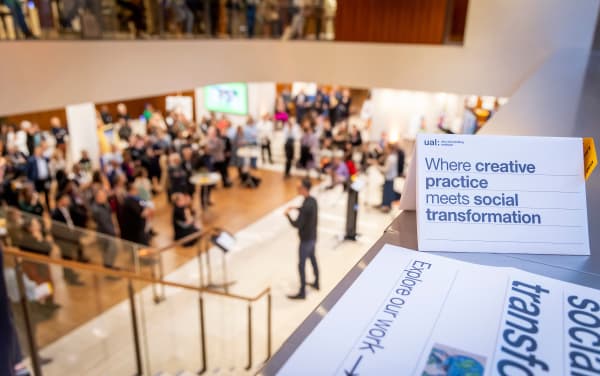 A leaflet propped on a surface, viewed from a high point during an event, performers and viewers can be seen in the background