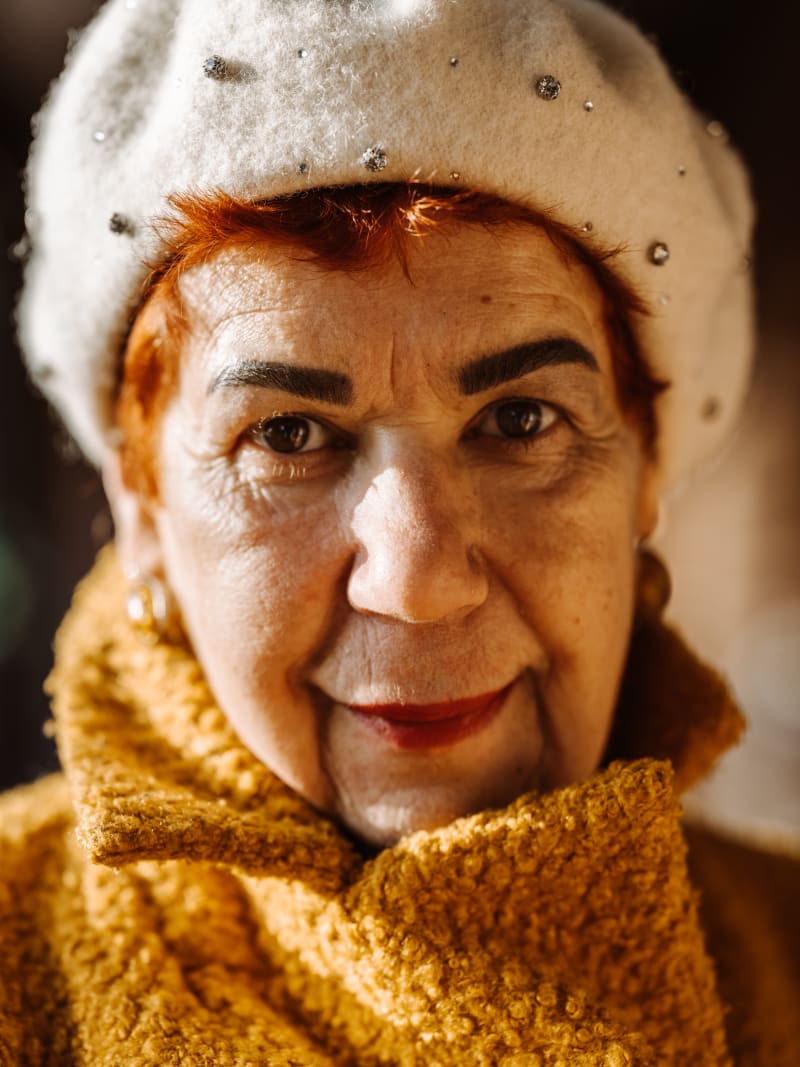 We see an older lady, dressed in a warm orange coat looking straight at the camera.